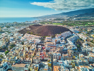 Fototapeta premium Drone view of a volcanic hill surrounded by residential neighborhoods, resort buildings, and coastal landscape in Tenerife, Canary Islands, Spain