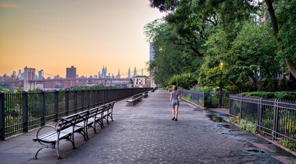 Peaceful riverside walkway with Brooklyn Bridge and Manhattan skyline at sunset in New York City