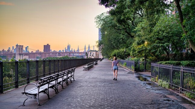 Peaceful riverside walkway with Brooklyn Bridge and Manhattan skyline at sunset in New York City