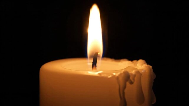 Close-up of a lit candle with flickering flame against a black background, perfect for a calming or memorial video
