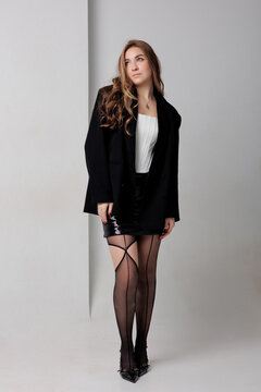 Young woman poses in black blazer with sheer tights in studio setting during afternoon light
