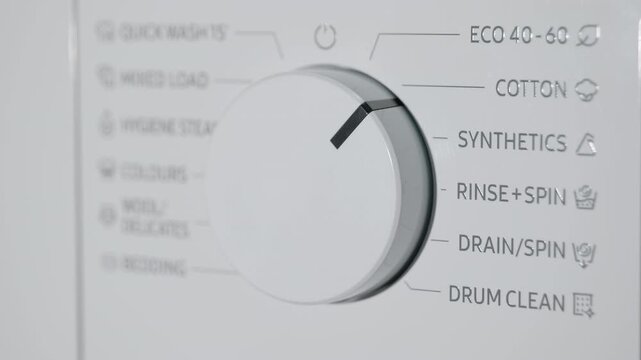 Hand turning the program dial on a washing machine. Close-up of a person's hand turning the selector dial on a modern washing machine to choose a laundry cycle, representing household chores