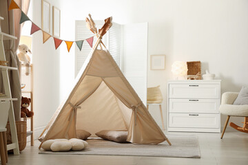 Stylish toy wigwam, furniture, pillows and decor in light playroom. Interior design © New Africa