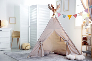 Stylish toy wigwam, furniture, pillows and decor in light playroom. Interior design © New Africa