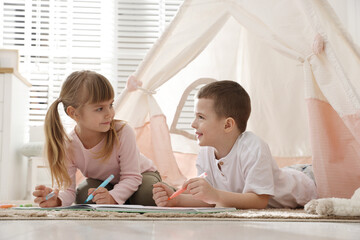 Little kids drawing in sketchbook together near toy wigwam at home © New Africa