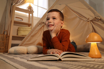 Little boy reading book near toy wigwam at home © New Africa