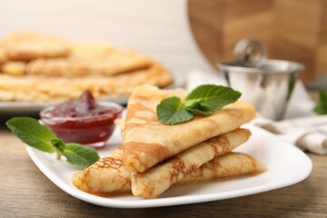 Tasty crepes with mint leaves and jam served on wooden table, closeup © New Africa