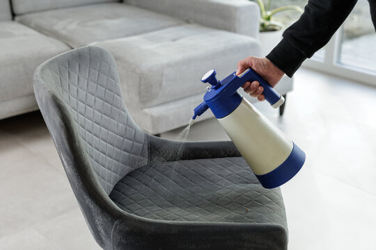 Spraying cleaning solution on upholstered chair for stain removal and fabric care