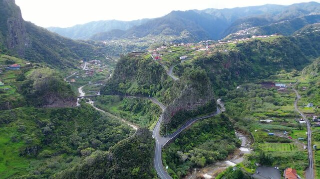 Dramatic aerial view of Madeira's verdant valleys and winding mountain roads, showcasing the island's unique landscape and charming hillside communities. Faial