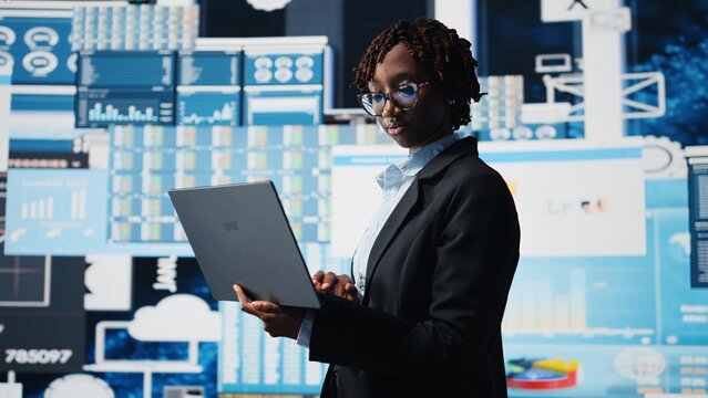 Manager using laptop software to compare company metrics on digital videowall before making decisions. Entrepreneur analyzing key performance indicators using notebook program, camera A