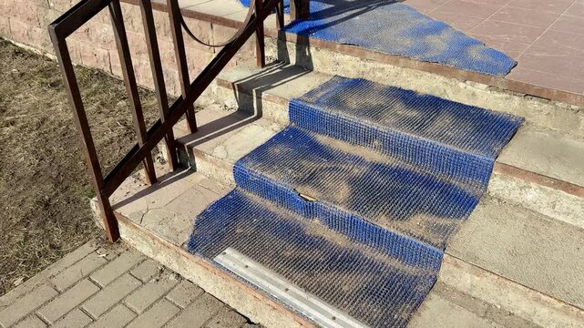 Worn blue anti slip stairs outdoors, scuffed textured coating on concrete treads, metal nosing at base, rusted railing casting long.