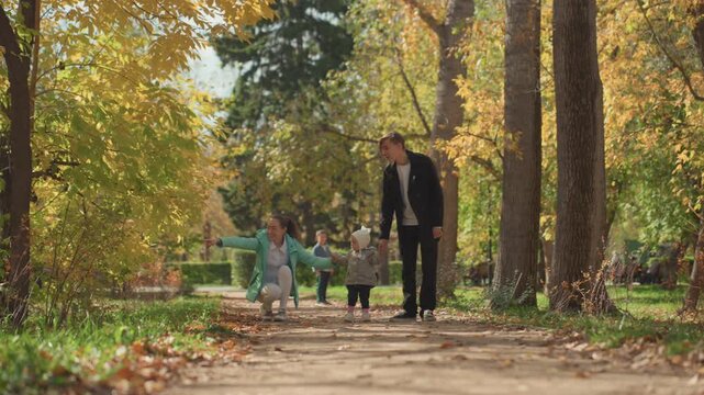 White father walking with children along treelined autumn path, golden leaves and soft sunlight, father playing with daughter while toddler toddles beside, candid family marriage moment, reflective