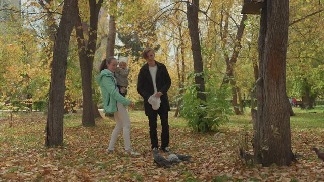 Autumn park couple playful feeding pigeons. Partners toss breadcrumbs to curious birds under golden trees, laughing together among fallen leaves casual coats, close conversation and warm smiles