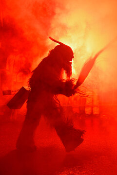 Scary silhouette of a Krampus demon in red smoke and fire light at night.