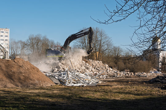NARVA, ESTONIA - MARCH 24, 2026: A Volvo excavator dismantling concrete structures with dust rising in the air. The Orthodox Church of Saints Cyril and Methodius is seen in the background.