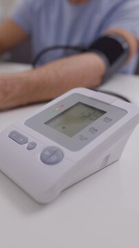 Vertical macro shot of an electronic blood pressure monitor display with changing numbers during a medical checkup.