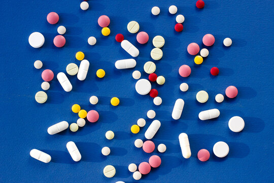 Tablets and pills of different colors and sizes on a blue background. Pharmacology and medicine