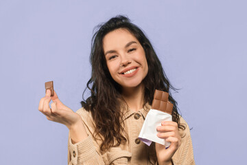 A woman stands against a plain background while holding chocolate bars. She smiles happily as she...