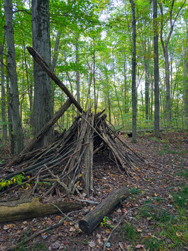 A crude lean-to of branches and sticks stacked in a heap stands near a trail in the woods in an Ohio park, seen at dusk.