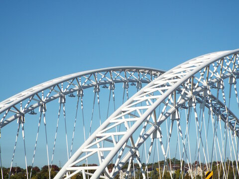 The white arches and suspension cables of the Vimy Memorial Bridge stand prominently against a clear blue sky.
