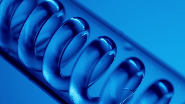 Blue liquid chemicals moving through glass spiral in lab on neon background.