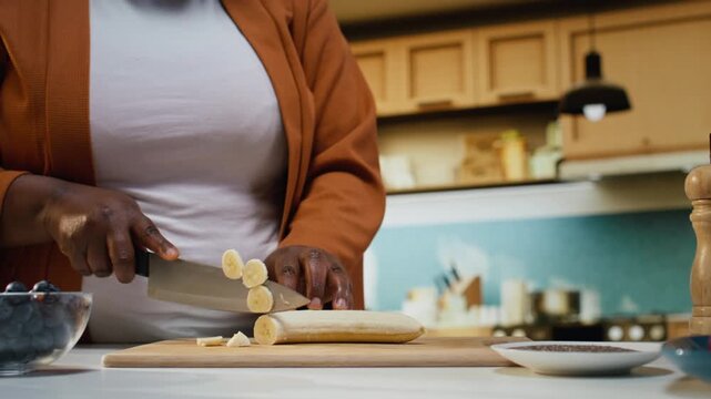 Close up of vlogger chopping banana for chia bowl recipe with yogurt, fruits on cutting board for chia pudding during food video. Filming step by step tutorial with nutritious breakfast idea.
