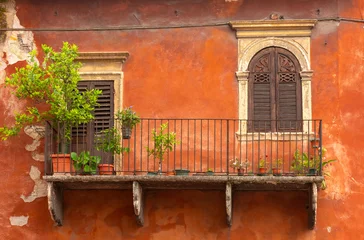 Old balcony with potted plants and wooden shutters on weathered orange facade in Verona, Italy. © Kavalenkava
