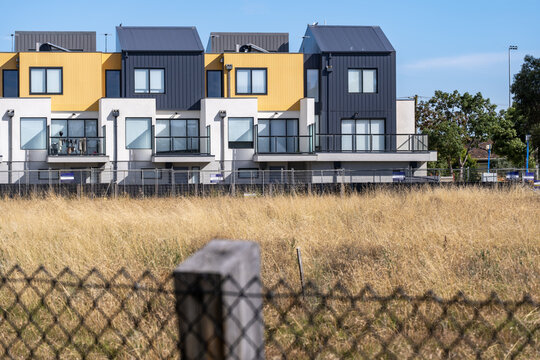 Modern townhouses behind a dry grassy field in suburban Australia. Contemporary residential development contrasting with undeveloped land. Urban expansion, housing growth, real estate