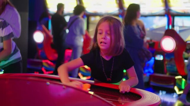 Focused girl playing air hockey game reaching for puck on bright arcade table enjoying competitive and fun atmosphere with family and friends 