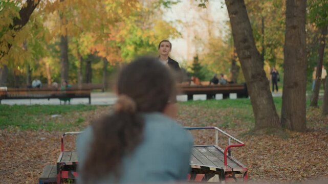 Park bench autumn proposal accepted, woman claps with joy. Intimate engagement moment shows couple celebrating acceptance on wooden bench, warm golden leaves, smiling partner and hopeful planning