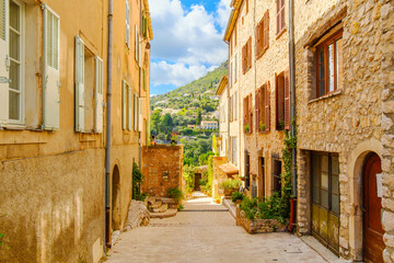 Obraz premium A narrow pedestrian alley through historic stone buildings leading to the outer wall and scenic views, in the charming old town center of the medieval hill town of Tourrettes-sur-Loup, France.