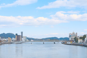 Fototapeta premium 穏やかな川面に架かる橋、水辺の街並みと遠景の山々