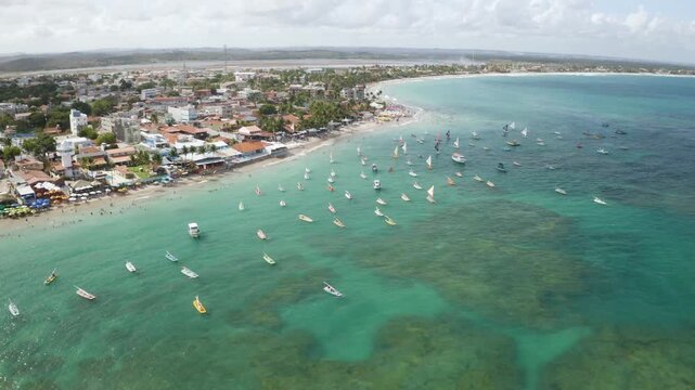4K drone view of Porto de Galinhas beach, Brazil, with turquoise water, boats and coastal town, showing tropical landscape and tourism.