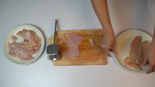 Top view of woman hands tenderizing chicken fillet with meat mallet on wooden board