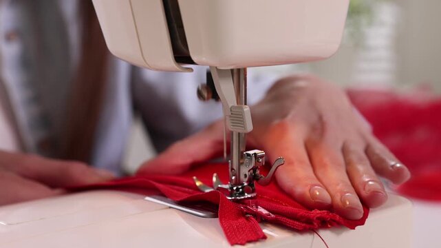 Woman sewing red fabric with professional machine in workshop, closeup