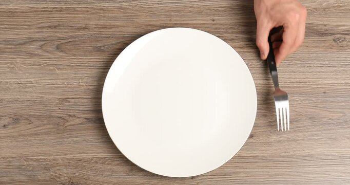 Man putting plate and cutlery onto grey table, top view
