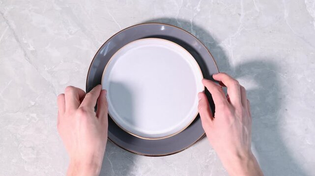 Man putting plates on light marble table, top view
