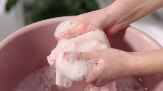 Woman washing stained kid's shirt in basinet at home, closeup