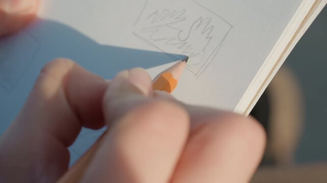 Closeup hands drawing small thumbnail, sunlit notebook filled with rough panel sketches and layout tests creative planner experiments with composition, quick strokes and mindful editing while testing