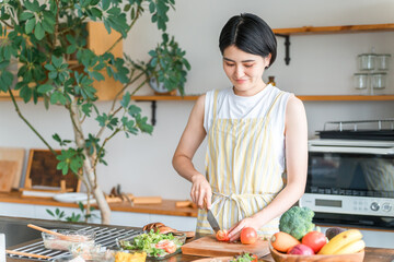 A young Asian woman cooking in the kitchen (cutting, using a knife, cooking, home-cooked meal)
