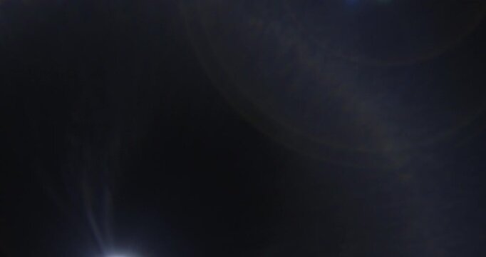 Sliding vintage noisy lens flare cinematic effect. Abstract dark background with moving light glare. Light source moves from side to side. Template for overlay design.