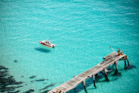 Clear turquoise water and boat floating by an old abandoned jetty, Althorpe Island, South Australia.