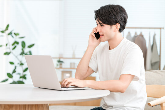 Japanese man working remotely from home, making a phone call on his smartphone (side job, meeting, working from home)