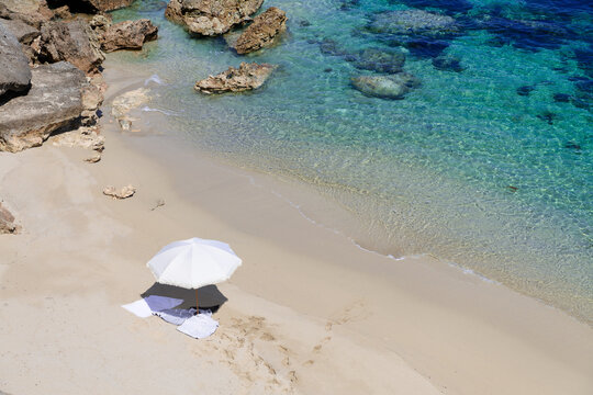 White umbrella at the beach with rocks and ocean close by, ready for a swim.