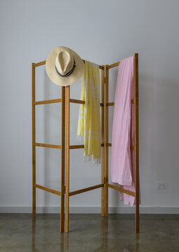 Wooden clothes dryer, with pink fabric and yellow fabric and sun hat draped over it