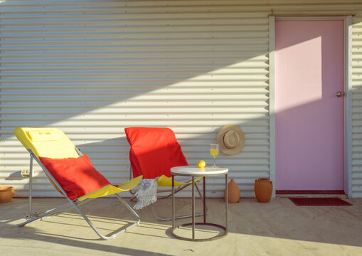 Pink door with yellow and red sun chairs and glass of wine.