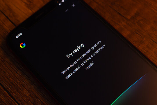 Mexico City, MEXICO - Mar 31 2026 : Smartphone displaying Google Assistant in dark mode, showing a "Try saying" prompt with a suggested multi-part voice query about a nearby grocery store and pharmacy