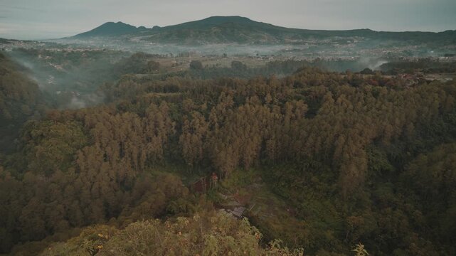 Cinematic misty forest mountain landscape during early morning with soft fog covering the valley. Filmed at Tebing Keraton, Bandung, West Java, Indonesia. Peaceful tropical scenery with lush greenery 