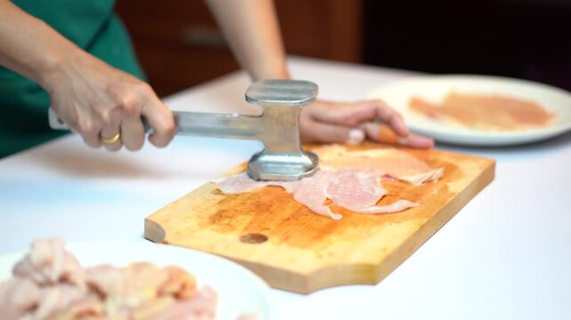 Woman Hand Using Meat Hammer To Tenderize Chicken Breast On Wooden Board