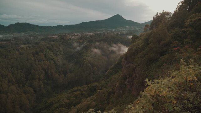 Cinematic misty forest mountain landscape during early morning with soft fog covering the valley. Filmed at Tebing Keraton, Bandung, West Java, Indonesia. Peaceful tropical scenery with lush greenery 
